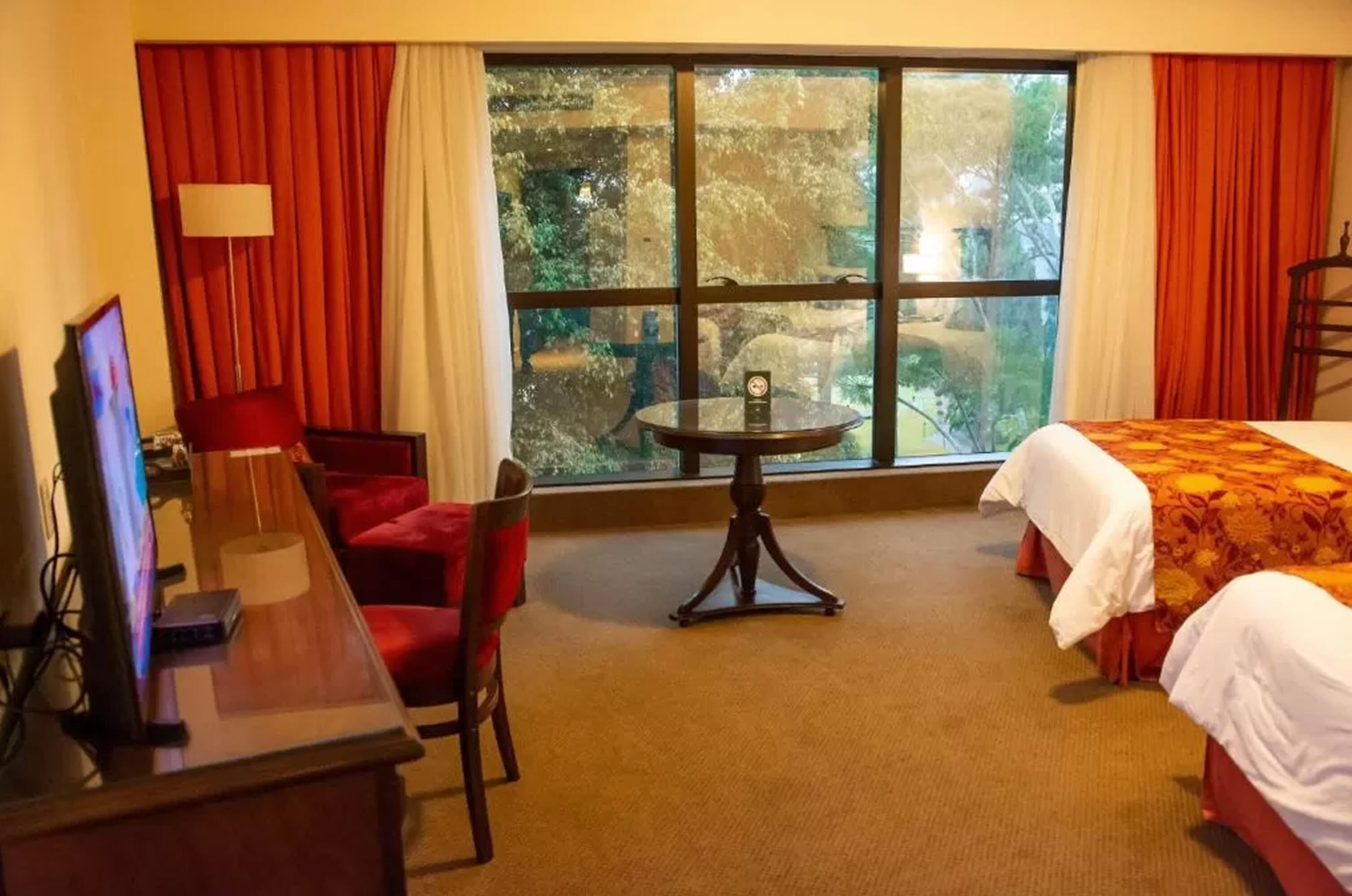 Una habitación de hotel con una cama, un escritorio con computadora, una silla, una mesa y un ventanal con cortinas.