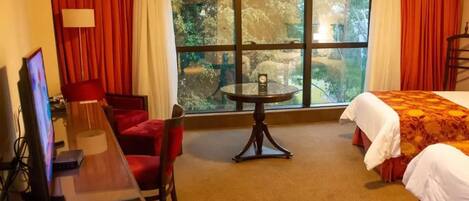 Una habitación de hotel con una cama, un escritorio con computadora, una silla, una mesa y un ventanal con cortinas.