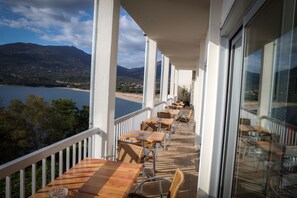 A balcony with tables and chairs overlooking a lake and mountains.