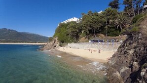 A beach with clear water, a sandy shore, and a building on a hillside. - Hôtel Roc e Mare (Propriano)