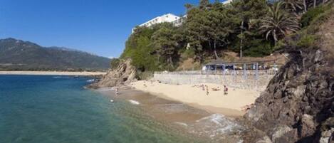 A beach with clear water, a sandy shore, and a building on a hillside.