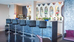 A bar area with multiple stools, a counter with various bottles, and a seating area with a sofa and cushions. - Hôtel Roc e Mare (Propriano)