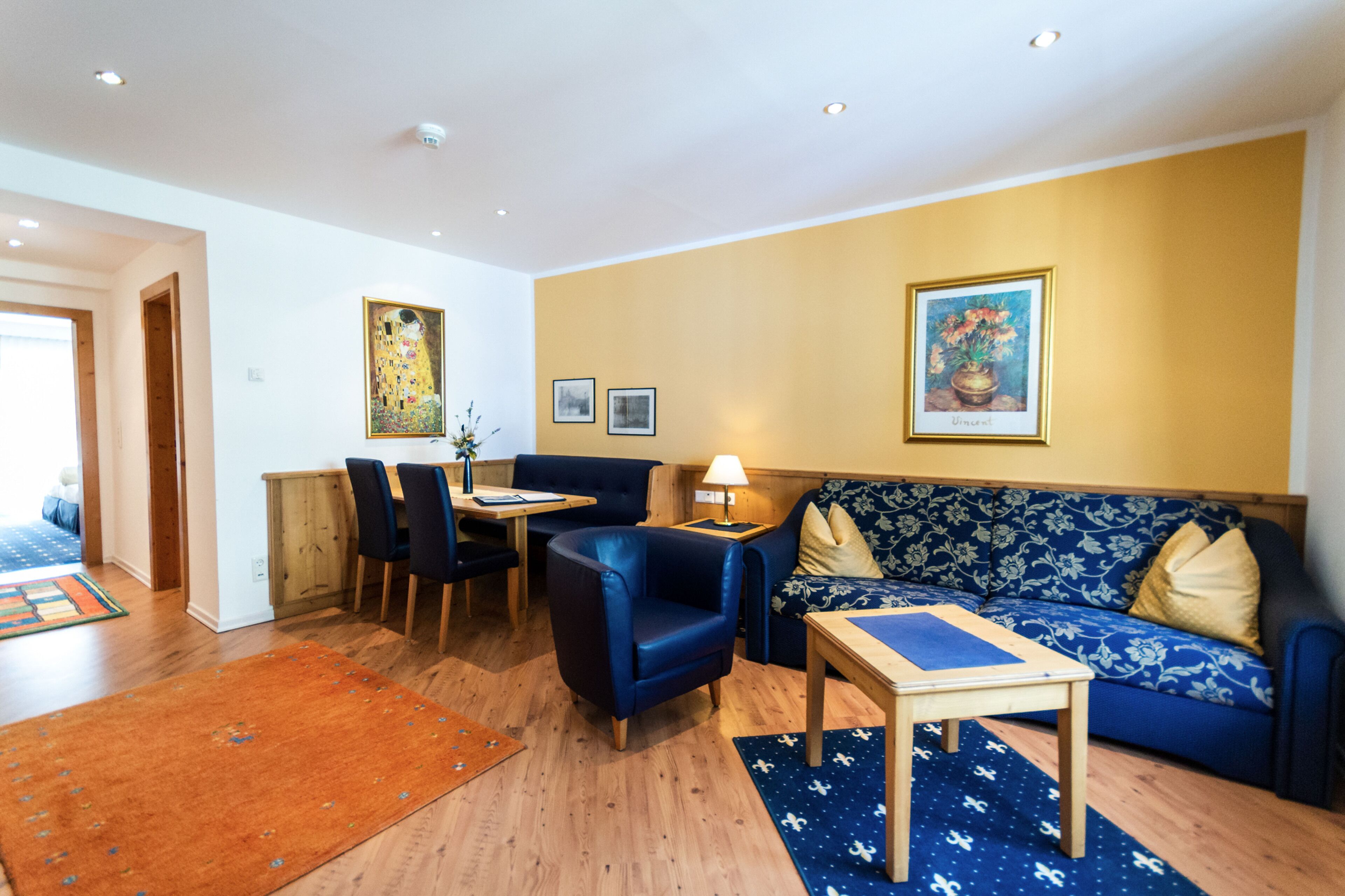 A living room with a sofa, chairs, a table, and artwork on the walls.