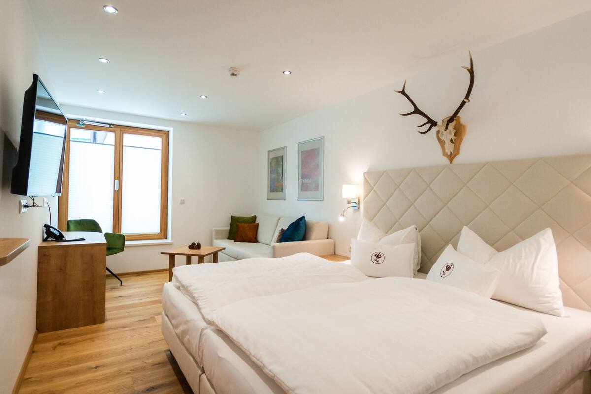 Een moderne hotelkamer met een groot bed, een bureau, een stoel, een televisie en een aan de muur bevestigde decoratie van een hert.