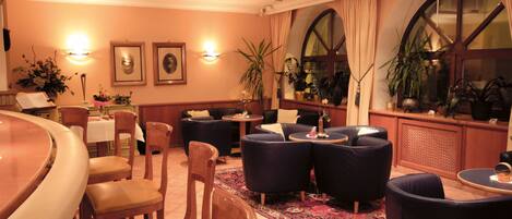 Un hall de hotel con una zona de bar, disposición de asientos y plantas decorativas.