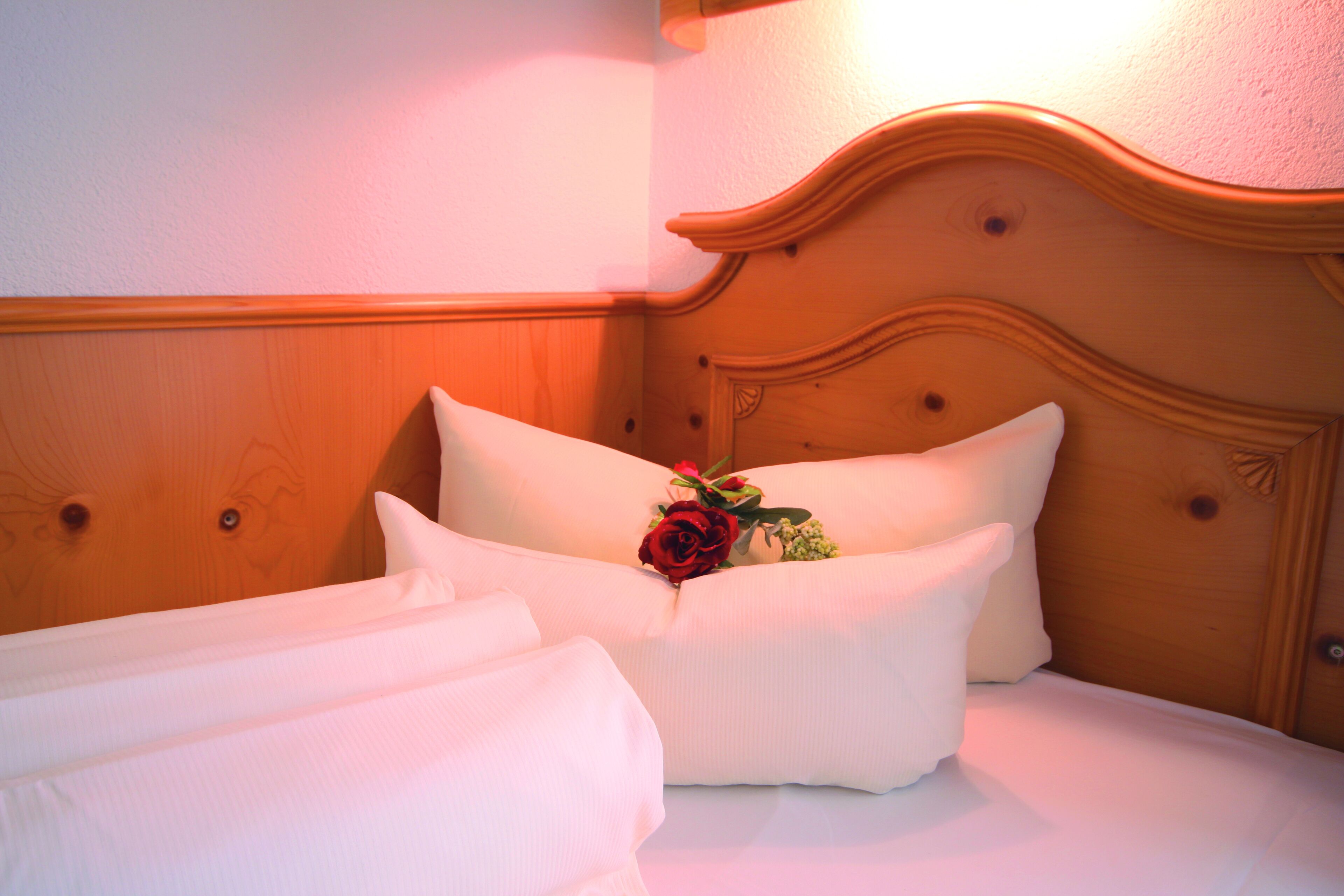 Ein Bett mit weißer Bettwäsche und einer roten Rosenblüte.