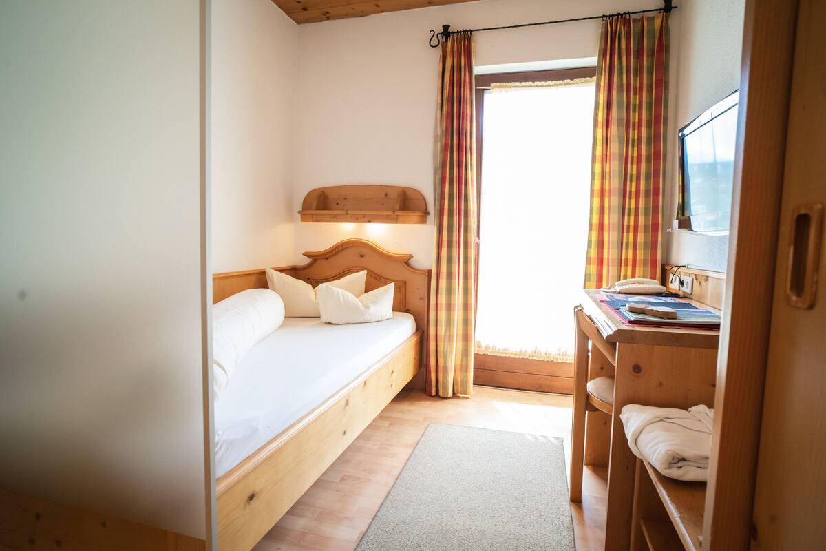 Een slaapkamer met een houten bed, een bureau en een raam met gordijnen.