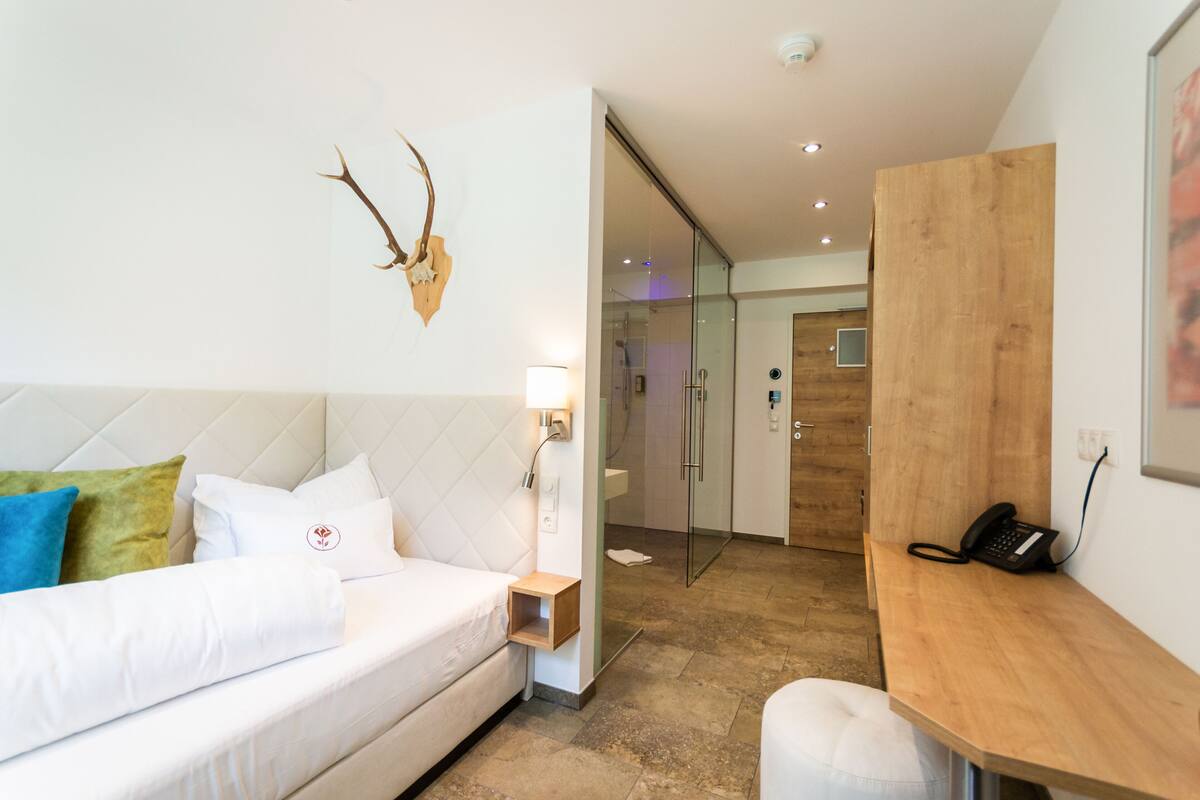Een moderne hotelkamer met een bed, nachtkastje en een houten bureau met een telefoon.