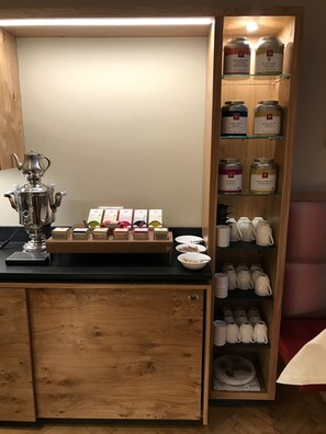 Un coin cuisine avec un meuble en bois, une théière en argent et divers produits alimentaires rangés sur des étagères.