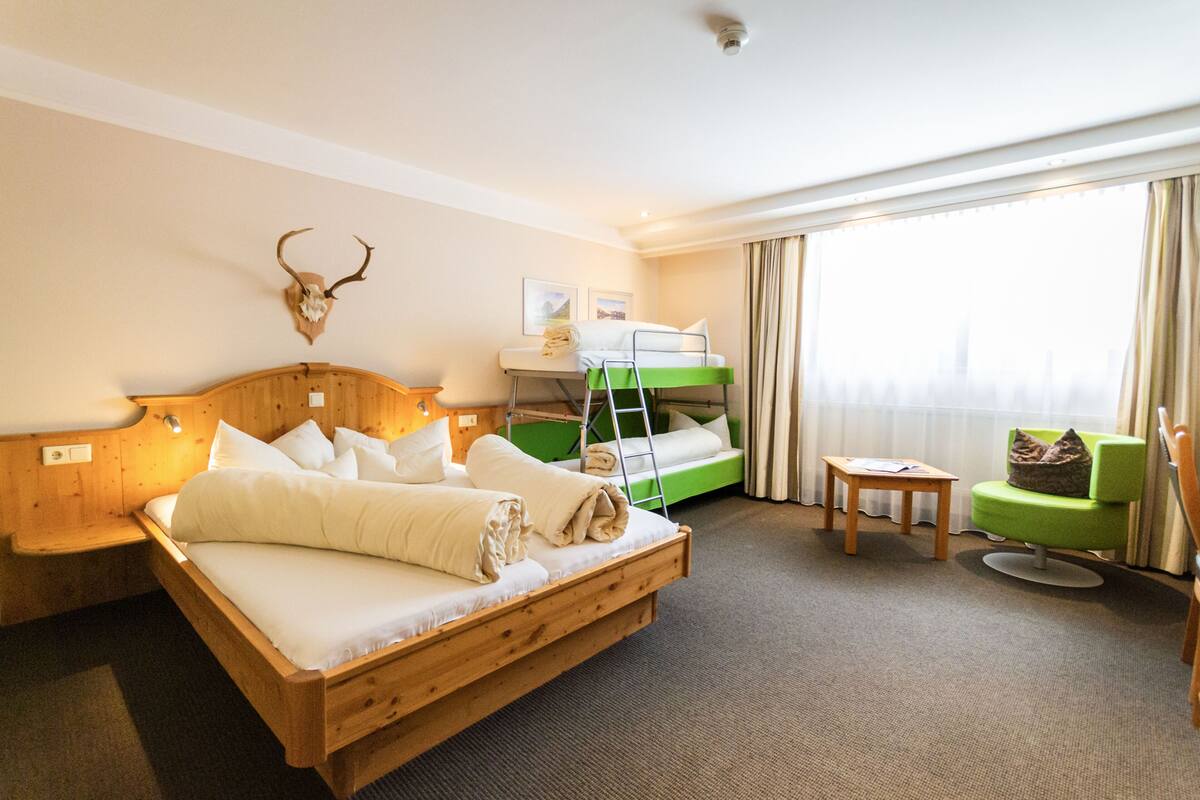 Een hotelkamer met een houten bed, een stapelbed, een groene fauteuil en een op de muur bevestigde herten schedel.