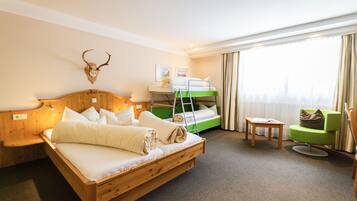 Een hotelkamer met een houten bed, een stapelbed, een groene fauteuil en een op de muur bevestigde herten schedel.
