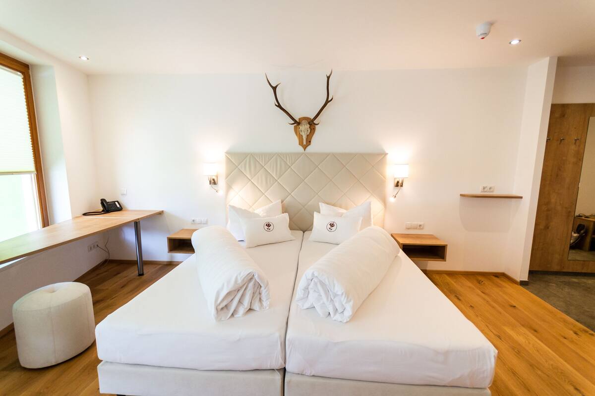 Een moderne hotelkamer met een groot bed, een houten bureau en een decoratieve geweihanger aan de muur.