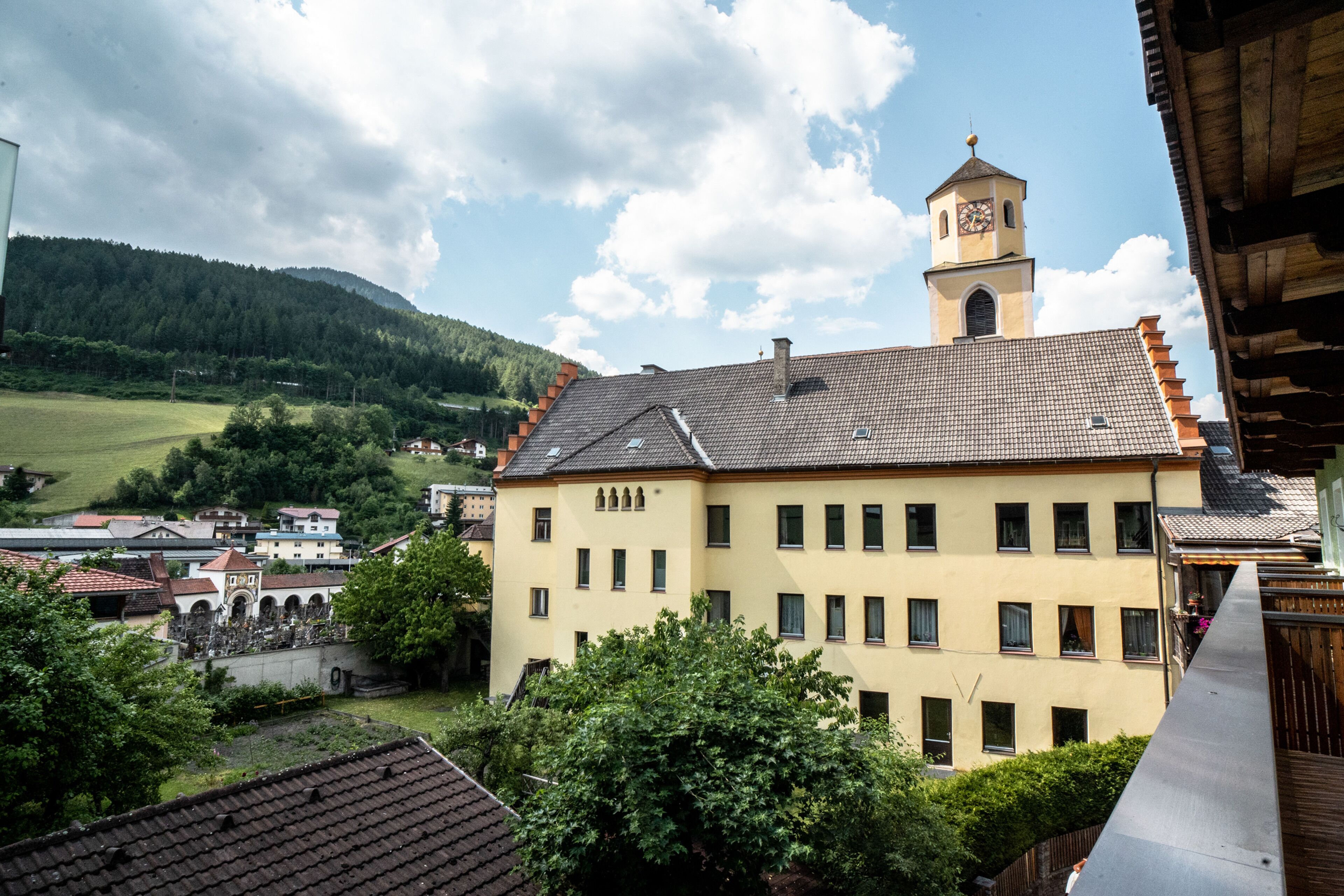 Ein gelbes Gebäude mit einem Glockenturm, umgeben von Grünflächen und weiteren Gebäuden.