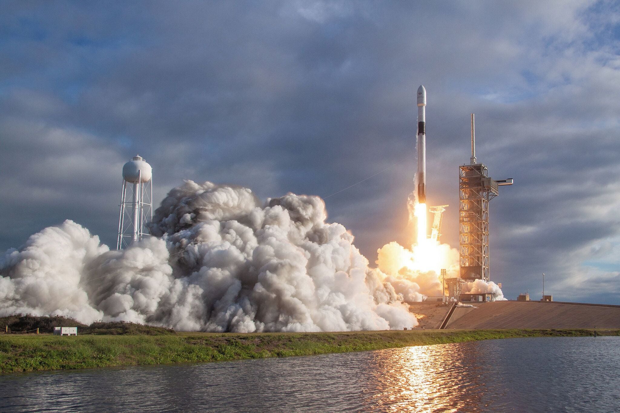 A rocket launch with smoke and flames, a water tower, and a launch pad.