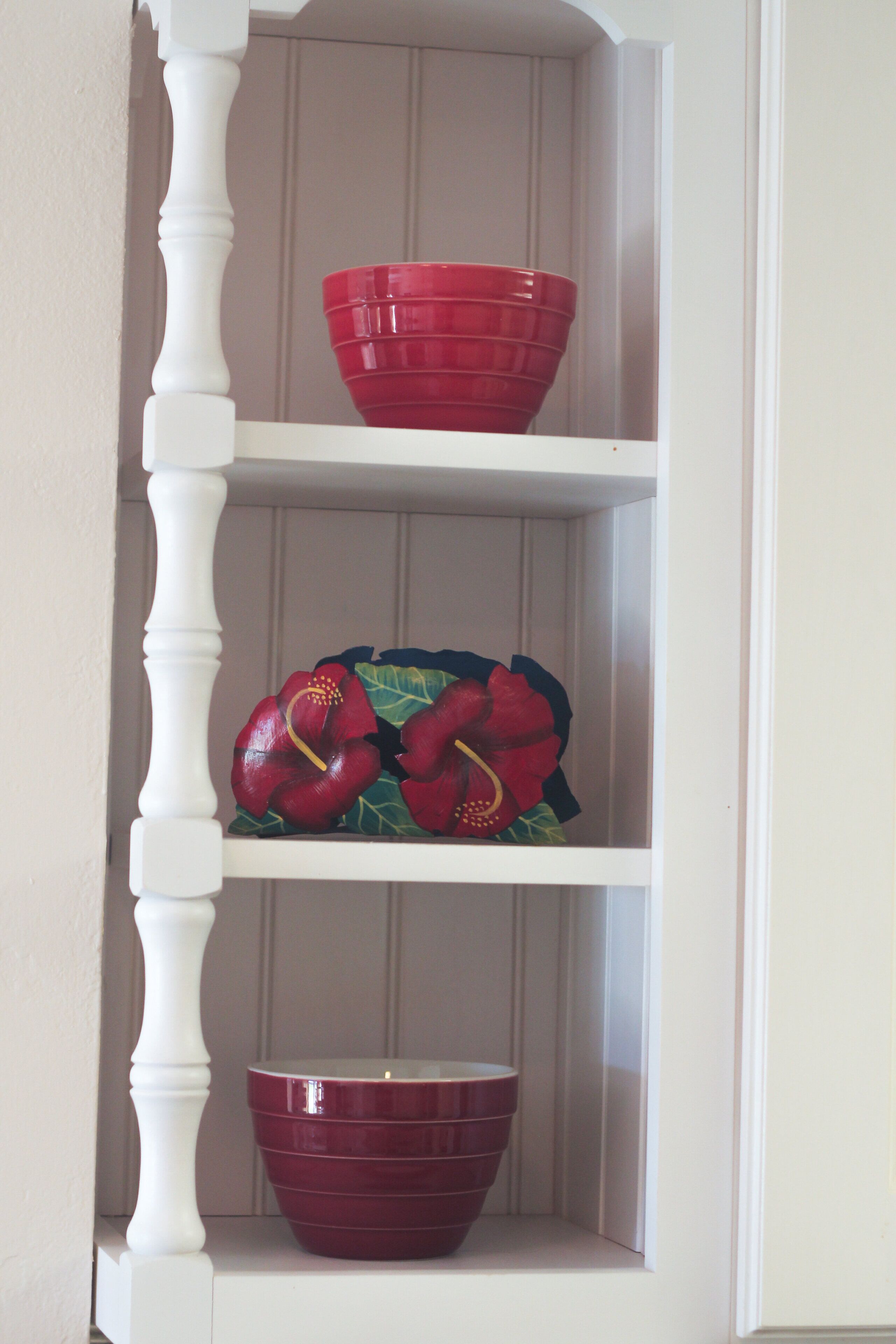 Una repisa blanca con tres cuencos rojos y dos flores artificiales rojas.