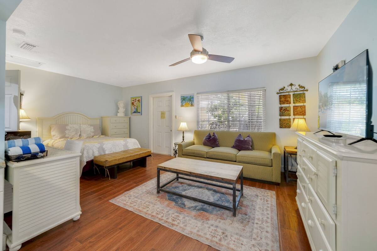 A well-lit room with a bed, a sofa, a coffee table, and a TV.