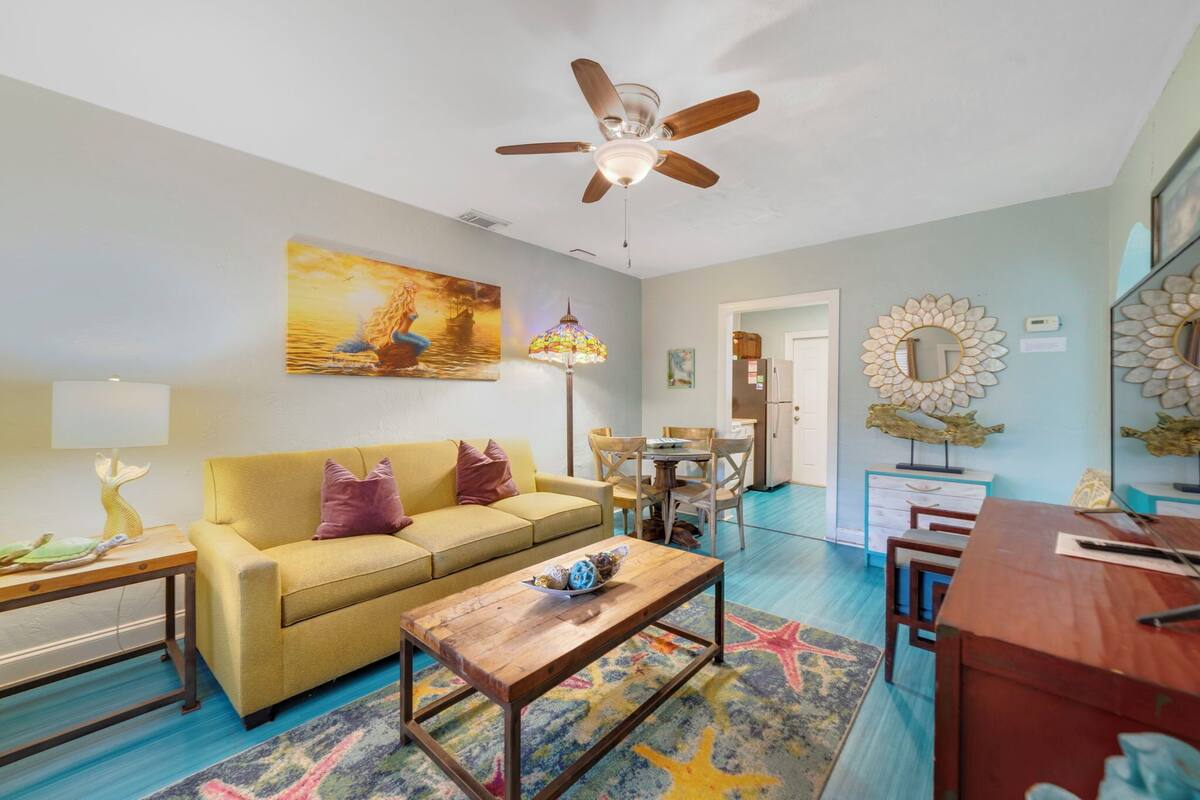 A living room with a yellow sofa, wooden coffee table, and a ceiling fan.