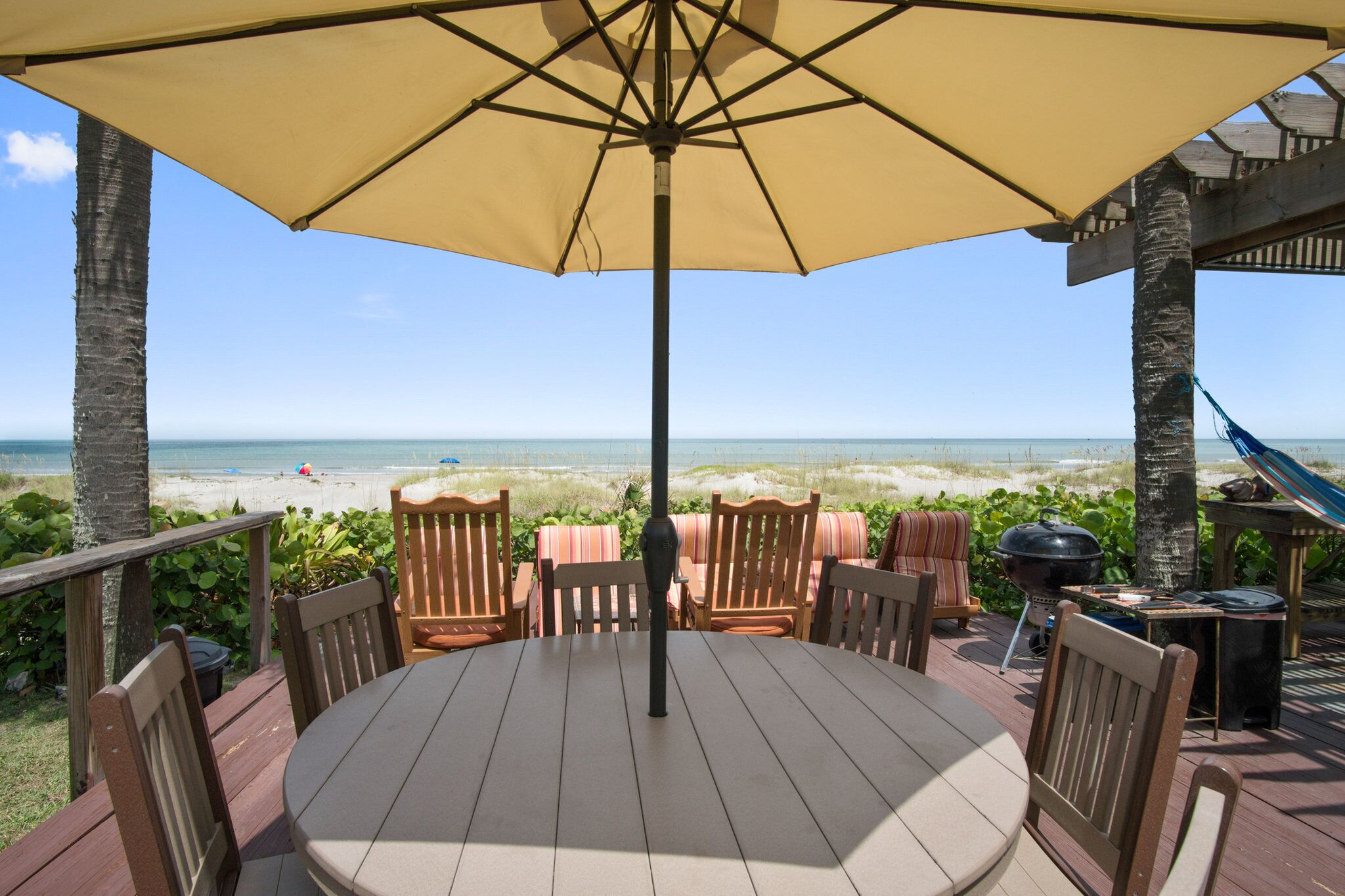 A deck with a round table and chairs, overlooking a beach.