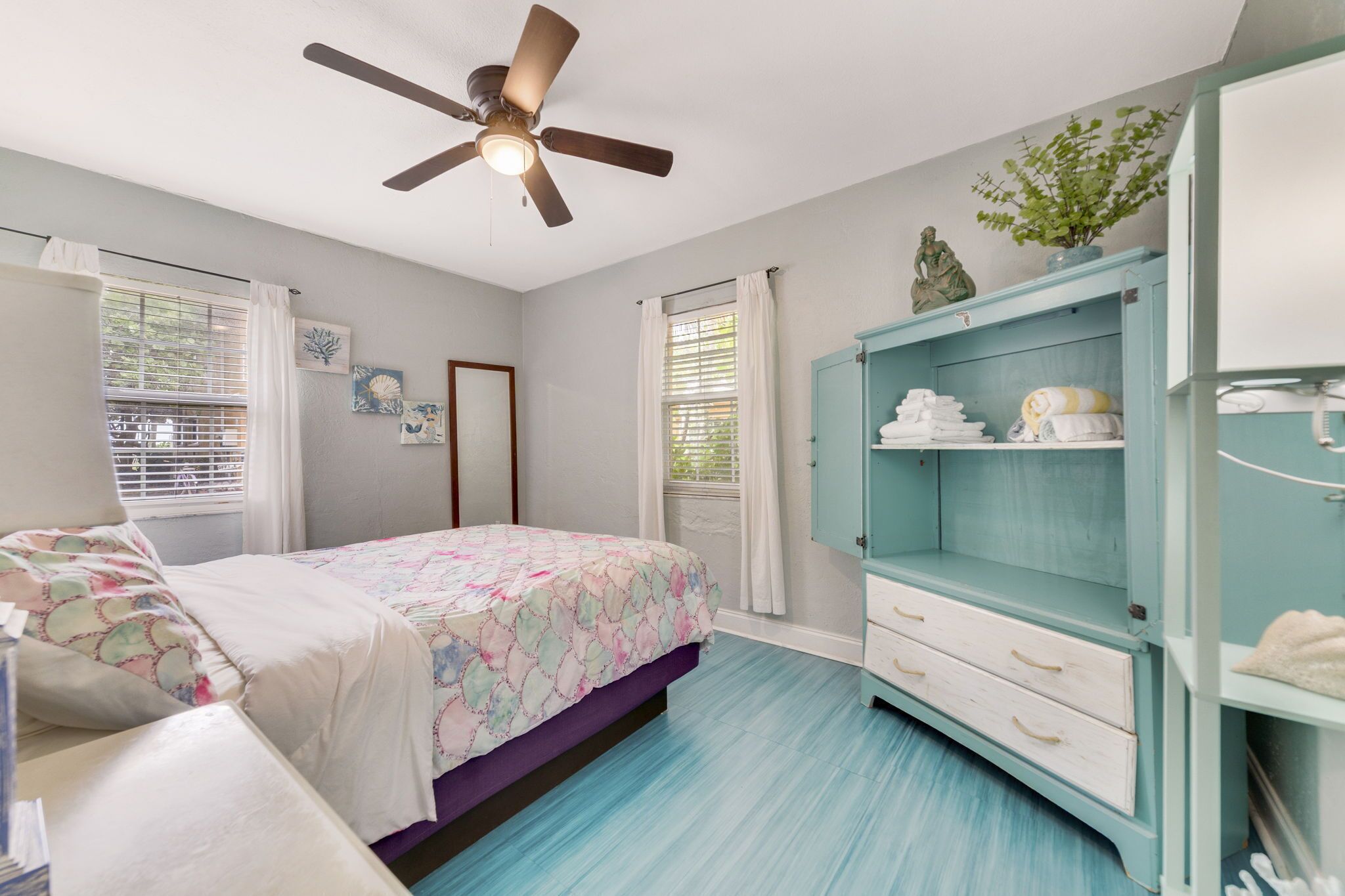 A bedroom with a bed, a ceiling fan, a wardrobe, and a window with curtains.