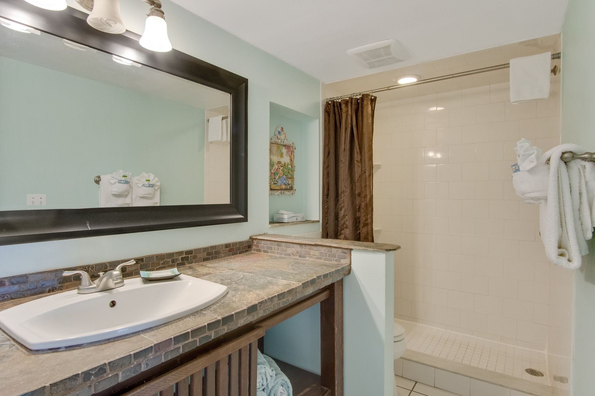 A bathroom with a sink, mirror, shower, and towel rack.