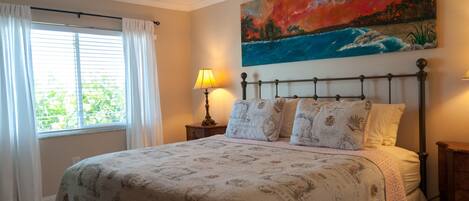 A bedroom with a bed, a painting, a ceiling fan, and a window with curtains.
