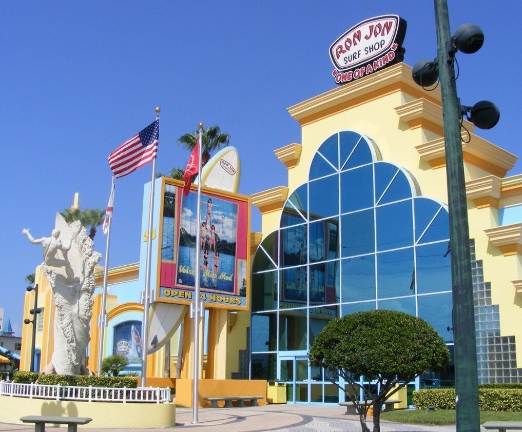 Un edificio con una grande facciata vetrata, un cartello con la scritta "Ron Jon Surf Shop" e una statua di una sirena.