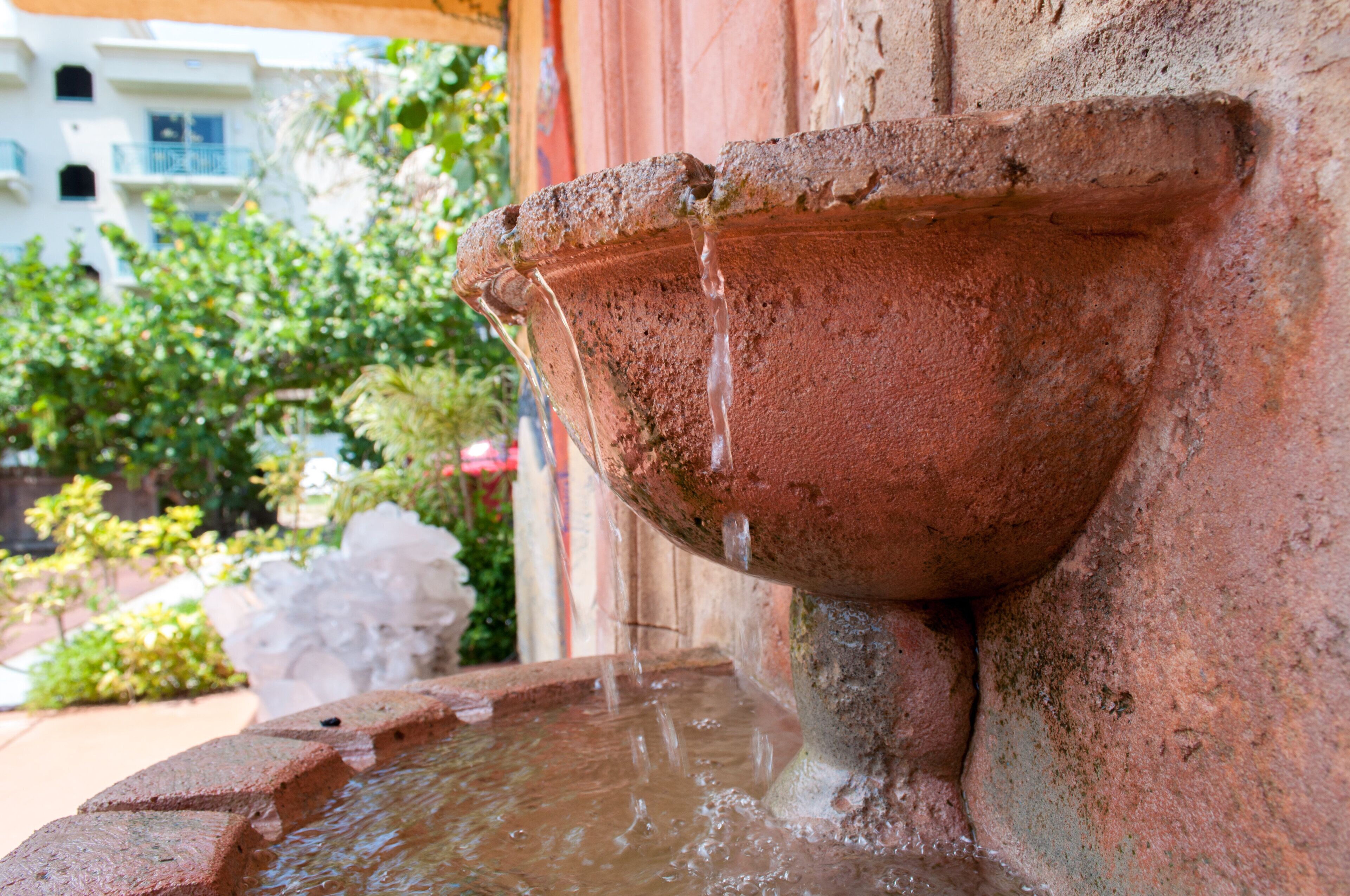 Una fuente de piedra con agua que fluye desde una cuenca, ubicada frente a un edificio de fachada de piedra.