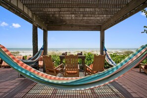 Een houten terras met een hangmat, stoelen en een tafel, met uitzicht op het strand.
