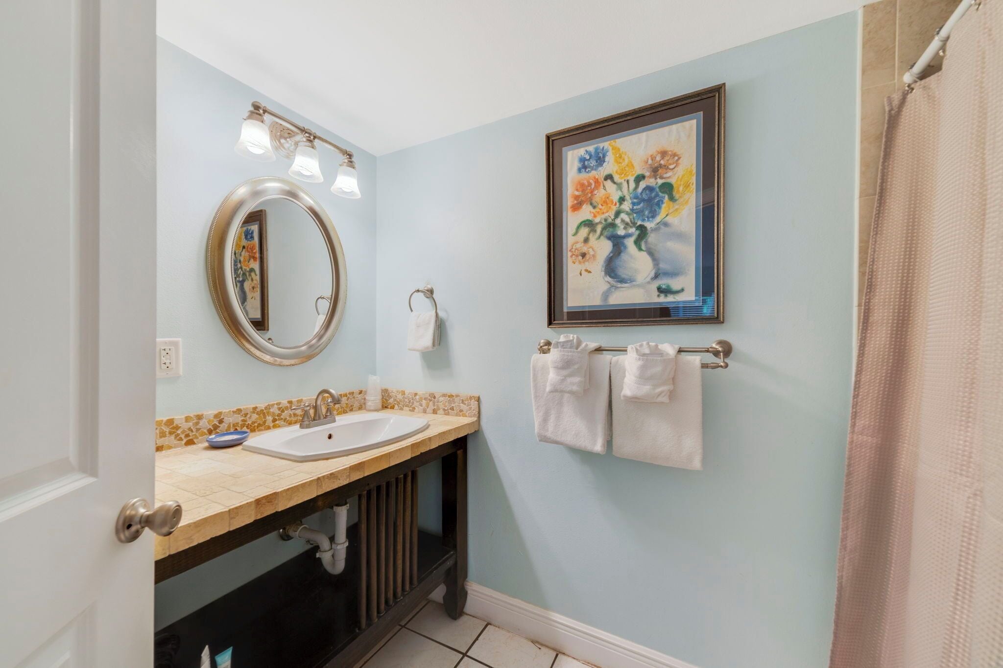 A bathroom with a double sink, a mirror, a framed floral painting, and a towel rack.