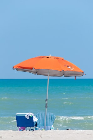 Een strandparasol, een blauwe strandstoel en een handdoek op het zand.