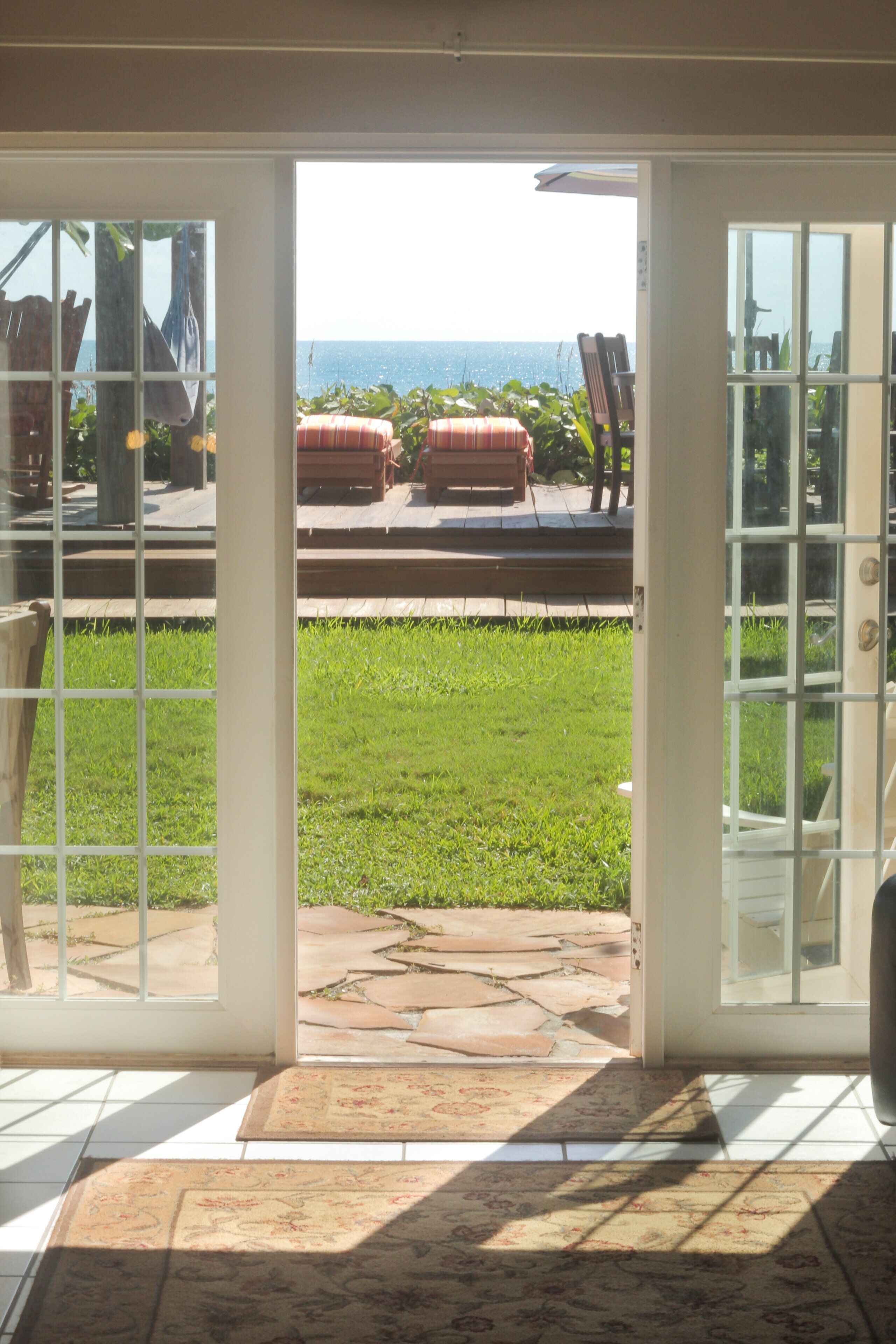 A view through a glass door leading to an outdoor patio with a stone floor, a grassy area, and a seating arrangement with a table and chairs.