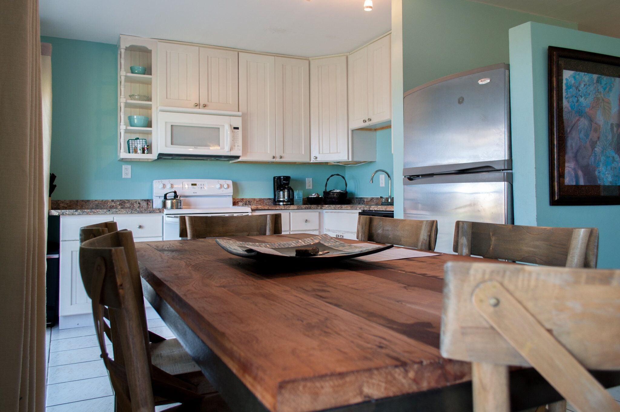 Una cocina con armarios blancos, una mesa de comedor de madera y un refrigerador de acero inoxidable.
