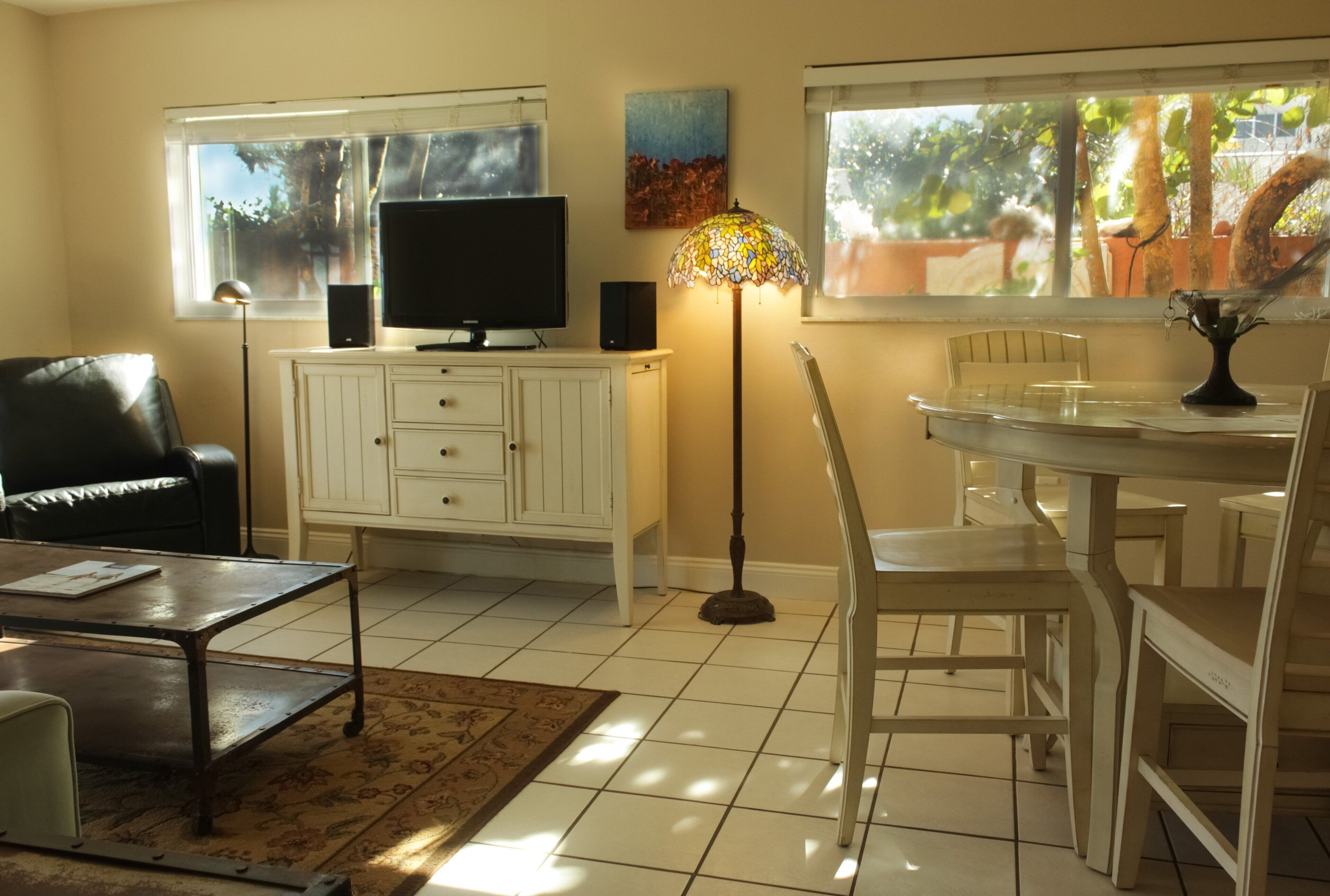 Una sala de estar con televisor, gabinetes blancos, lámpara, mesa de comedor y sillas.