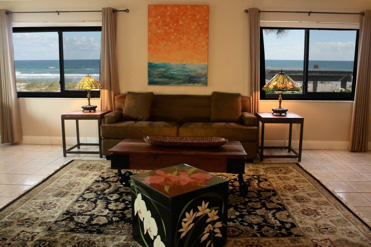 A living room with a sofa, two side tables with lamps, a coffee table, a rug, and a painting of a beach scene.