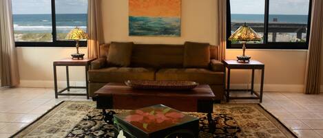 A living room with a sofa, two side tables with lamps, a coffee table, a rug, and a painting of a beach scene.