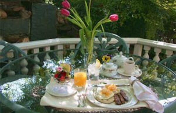 A round glass table with a breakfast setup including a teapot, cups, a plate with food, and a vase with flowers. - The Foxes Inn of Sutter Creek (Sutter Creek)