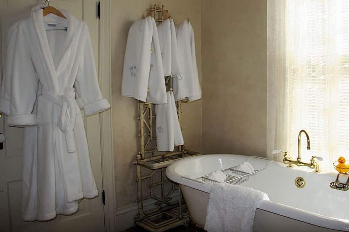 Ein Badezimmer mit einer Badewanne, einem Handtuchhalter mit mehreren Handtüchern und einem Fenster mit Vorhängen.