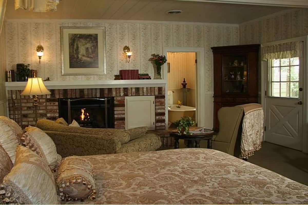 Ein traditionell eingerichteter Raum mit Kamin, einem Bett mit aufwändiger Bettwäsche, einer Sitzecke mit Tisch und einer Tür zu einem weiteren Raum.