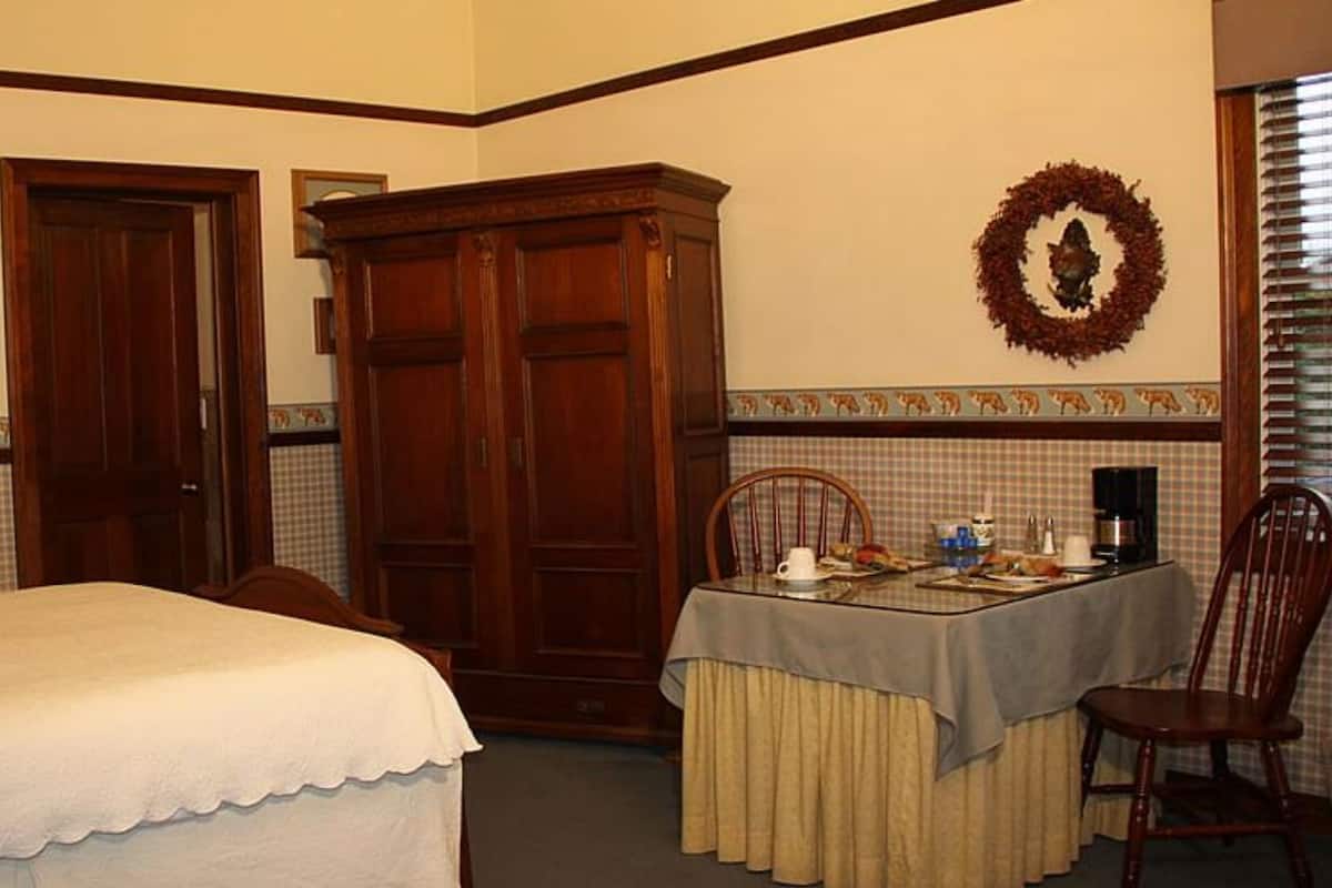 Ein Hotelzimmer mit einem Bett, einem Esstisch mit Stühlen, einem Holzschrank und einer Wand mit einem gerahmten Bild und einem Kranz.