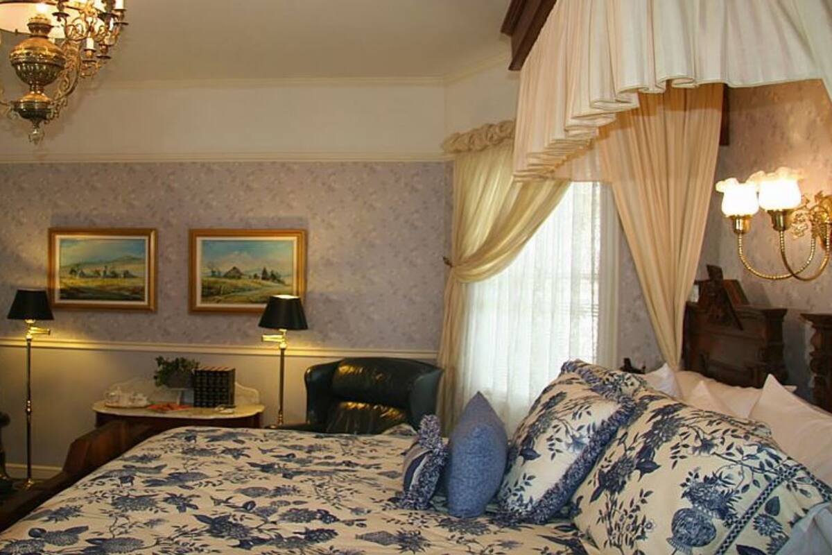 Ein Schlafzimmer mit einem großen Bett, zwei Wandlampen, einer Chandelüster und zwei gerahmten Landschaftsbildern.