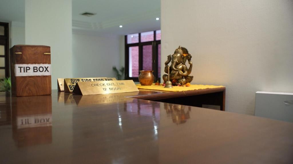 A reception desk with a wooden tip box, a small box labeled 'LIL BOX', and a sign indicating check-out time.
