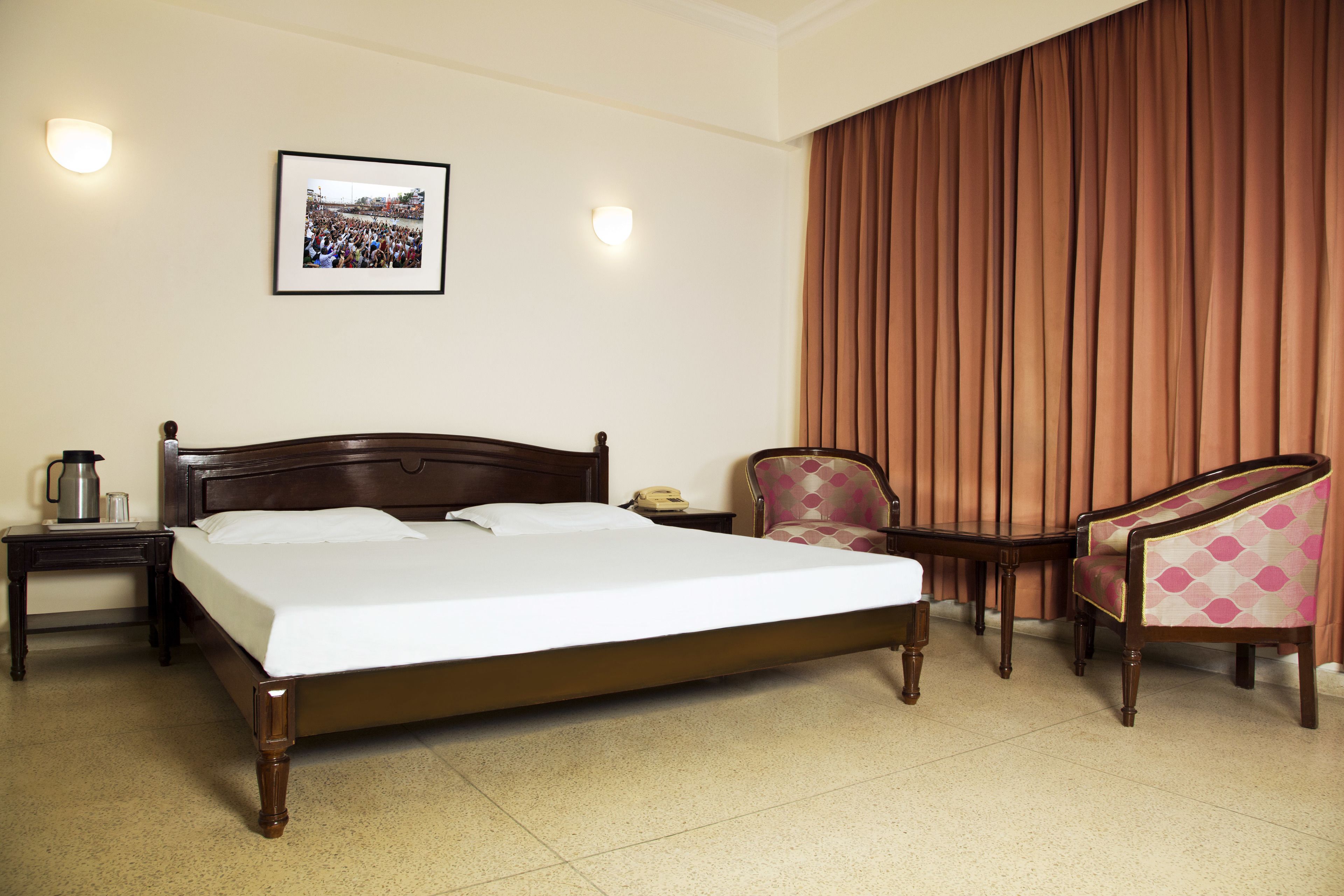 Habitación de hotel con una cama grande, una silla, una mesita de noche con lámpara y una fotografía enmarcada en la pared.