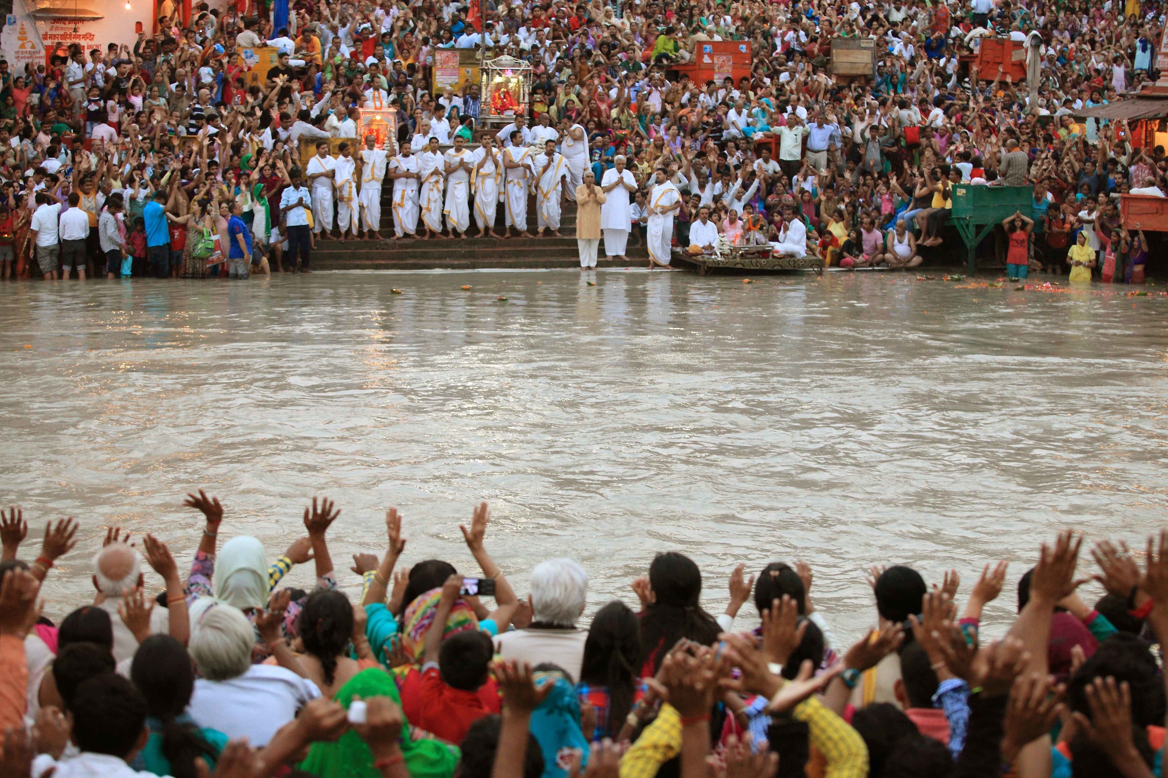 A large crowd gathered by a body of water, with people reaching towards the water's surface.