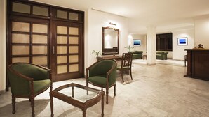 A spacious living area with a large wooden door, two green upholstered chairs, a glass coffee table, and a television in the background. - Alpana Hotel (Haridwar)