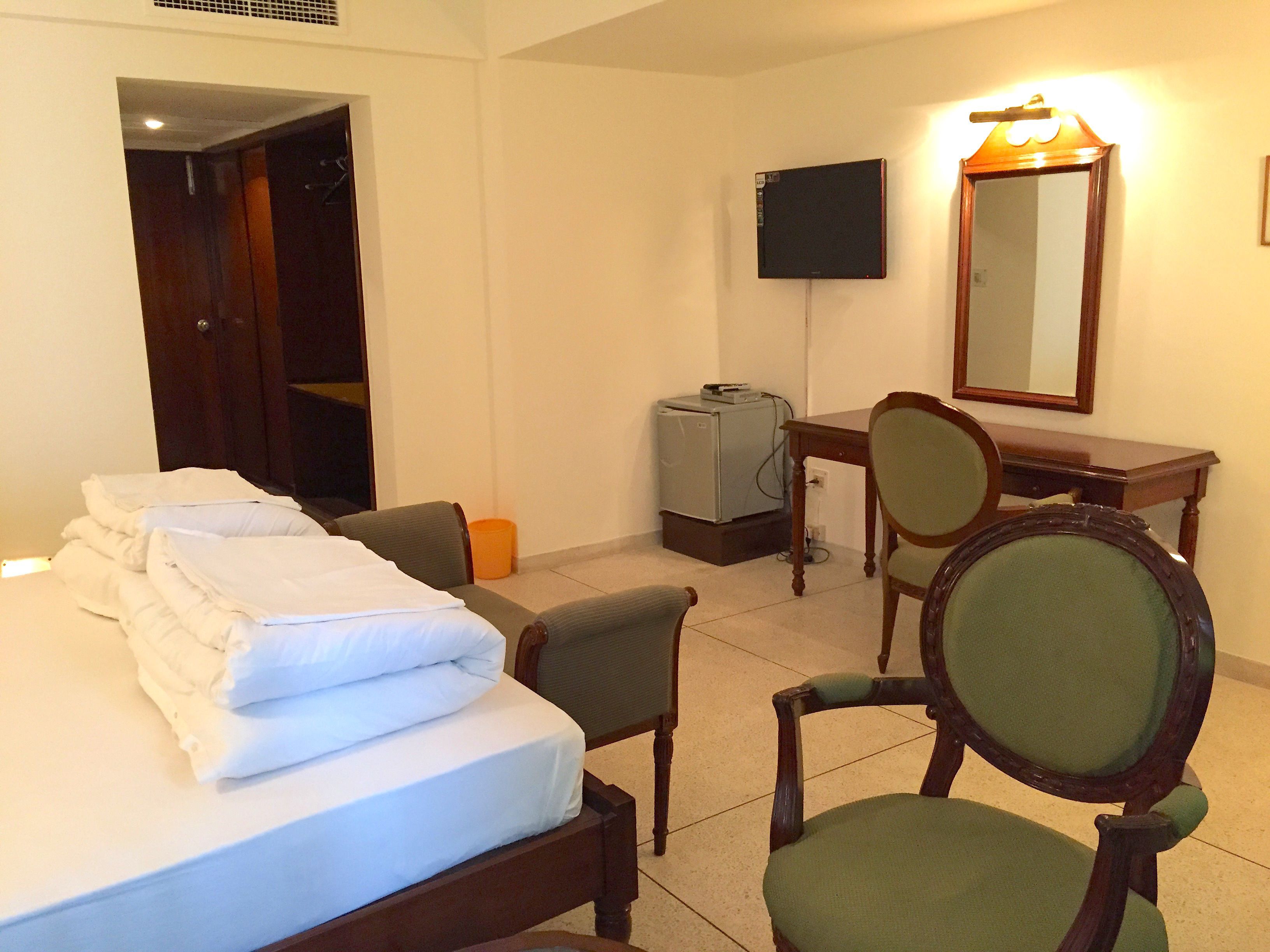 A hotel room with a bed, a desk, a chair, a television, and a refrigerator.
