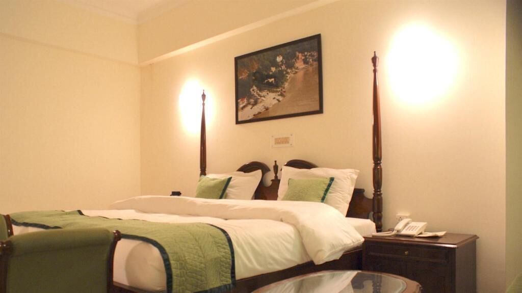A neatly made bed with green and white bedding, a bedside table with a lamp, and a painting on the wall.