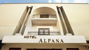 The exterior of the Hotel Alpana, featuring a prominent arched entrance, a balcony with decorative railings, and a clear sky above. - Alpana Hotel (Haridwar)