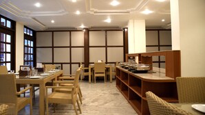 A dining area with a long table, wicker chairs, and buffet service. - Alpana Hotel (Haridwar)