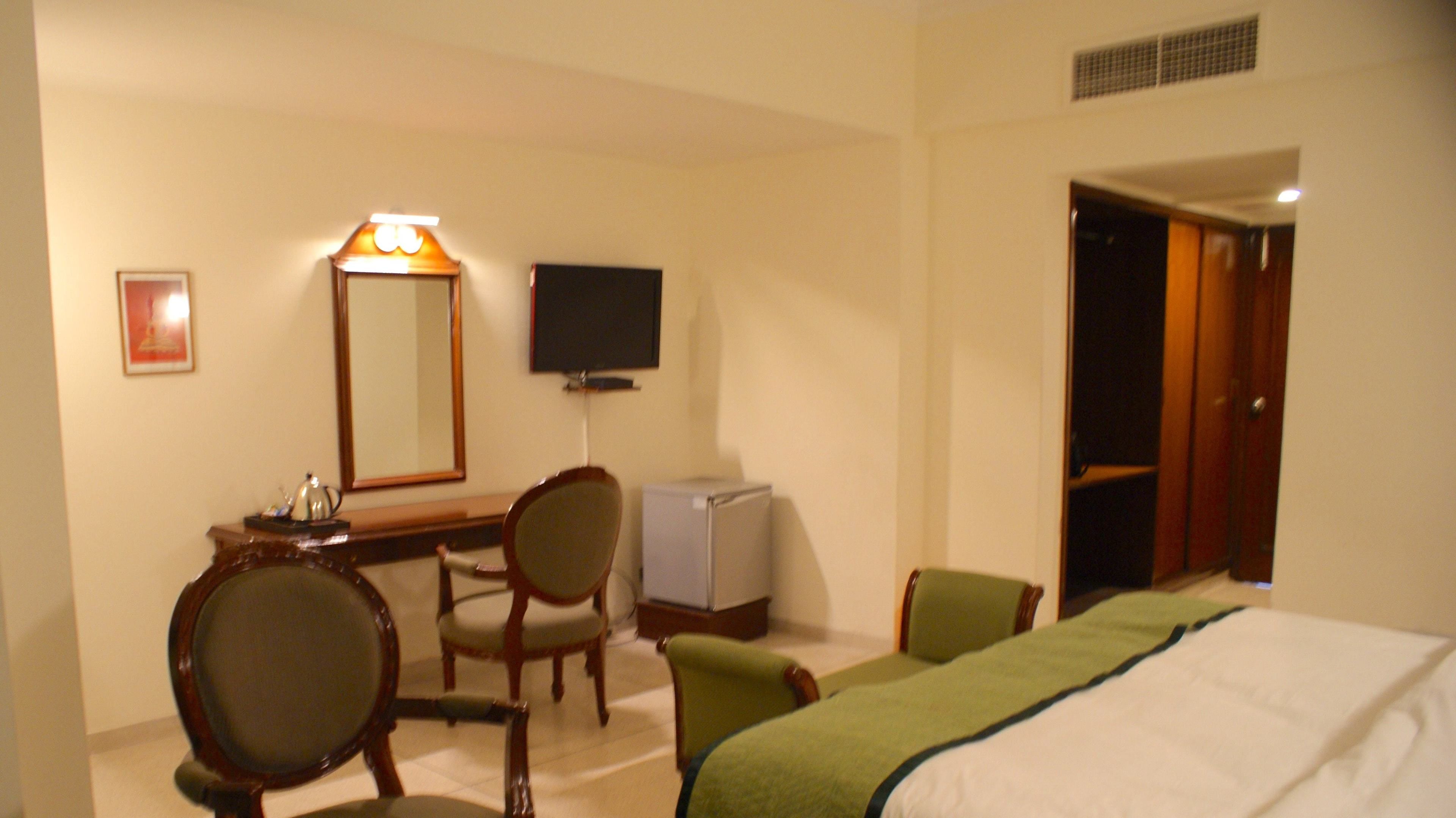 Een hotelkamer met een bed, twee stoelen, een bureau, een televisie en een spiegel.