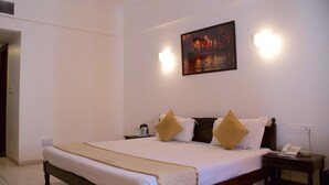 A hotel room with a large bed, a bedside table with a phone, and a painting on the wall. - Alpana Hotel (Haridwar)